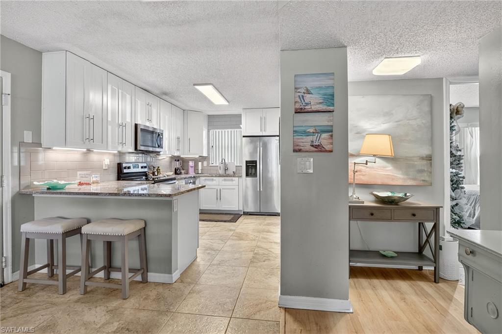Kitchen with a textured ceiling, stainless steel appliances, light stone counters, white cabinetry, and a kitchen bar