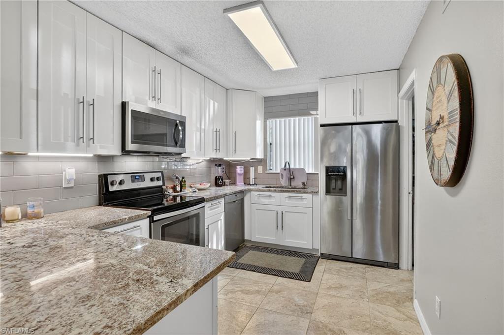 Kitchen featuring appliances with stainless steel finishes, white cabinets, backsplash, light stone countertops, and a textured ceiling