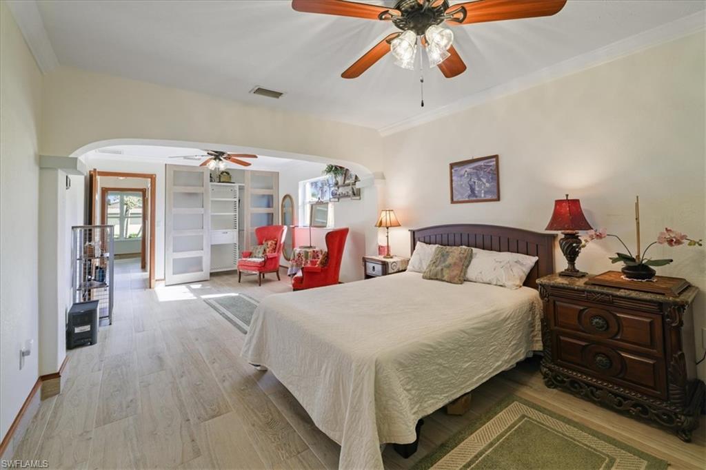 Bedroom with arched walkways, light wood finished floors, crown molding, and ceiling fan