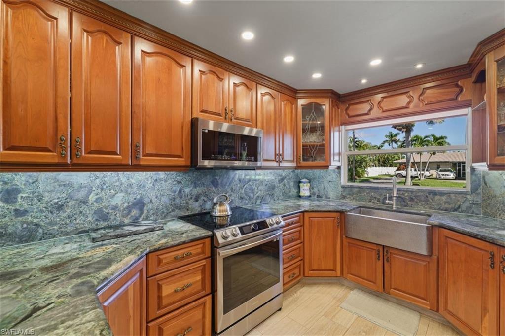 Kitchen with stainless steel appliances,  stone counters, glass insert cabinets, Cherry Wood cabinets, and backsplash