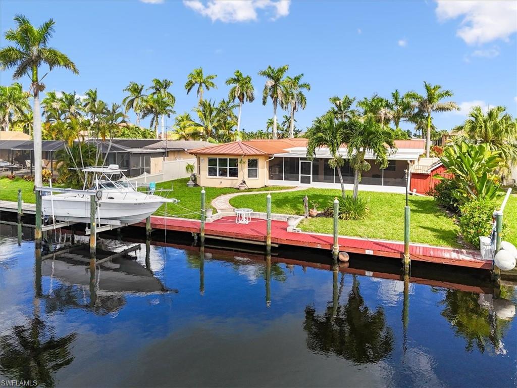 Dock featuring a sunroom, boat lift, a lawn, and a water view