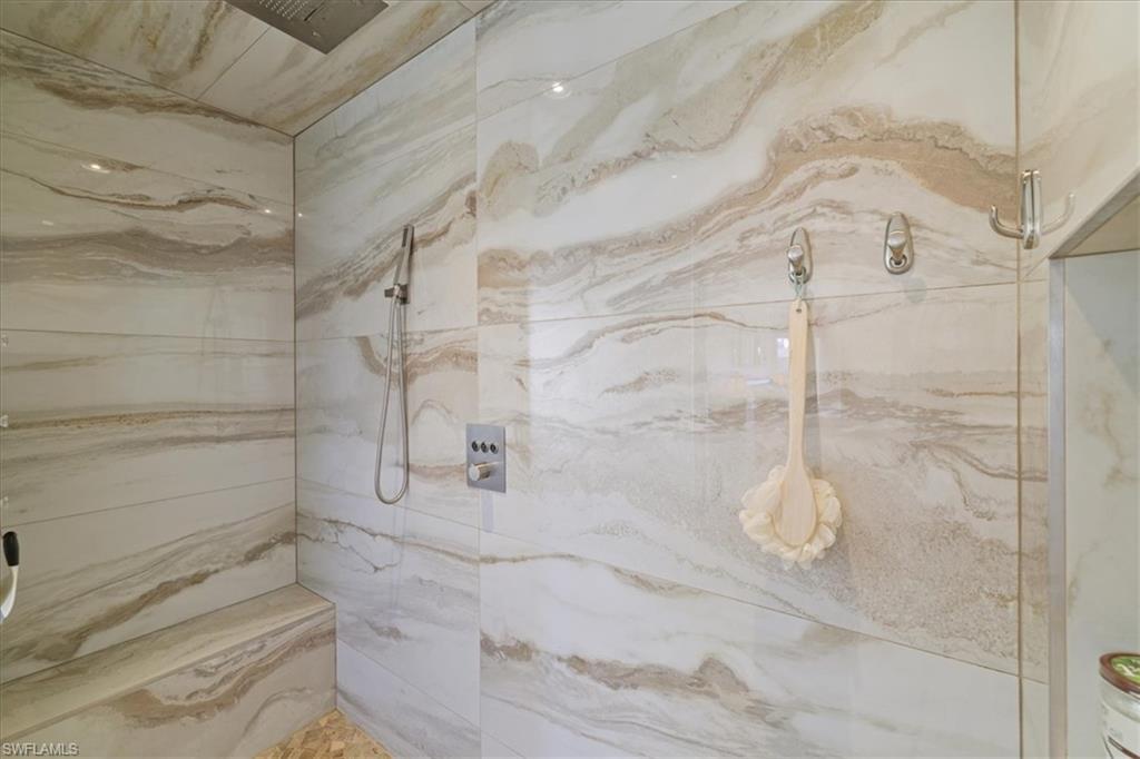 Bathroom featuring a marble finish shower with multiple shower heads and bench