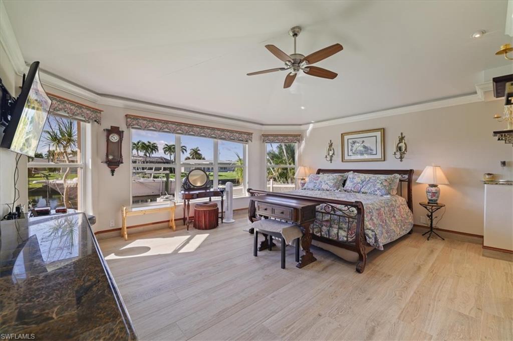 Bedroom with crown molding, light wood-style floors,  ceiling fan and wall of windows