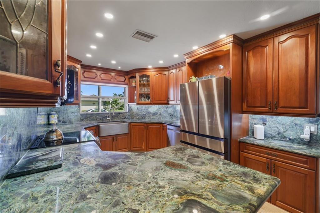 Kitchen featuring appliances with stainless steel finishes, glass insert cabinets, dark stone countertops, decorative backsplash, and recessed lighting