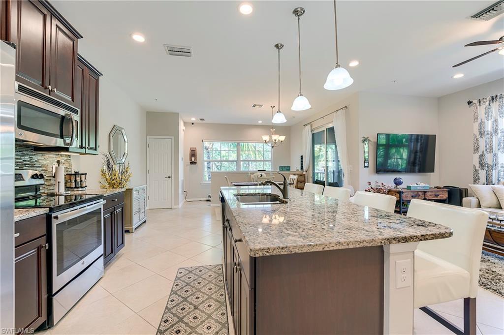 Kitchen featuring appliances with stainless steel finishes, dark brown cabinetry, light stone counters, a kitchen breakfast bar, and light tile patterned flooring