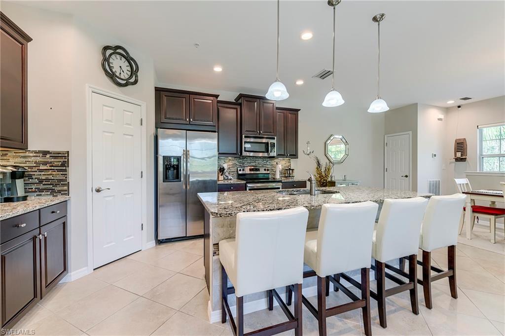 Kitchen featuring stainless steel appliances, dark brown cabinetry, light stone countertops, hanging light fixtures, and a breakfast bar area