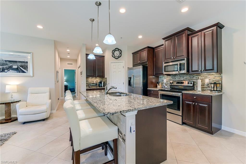 Kitchen featuring dark brown cabinetry, tasteful backsplash, appliances with stainless steel finishes, light stone countertops, and a kitchen breakfast bar