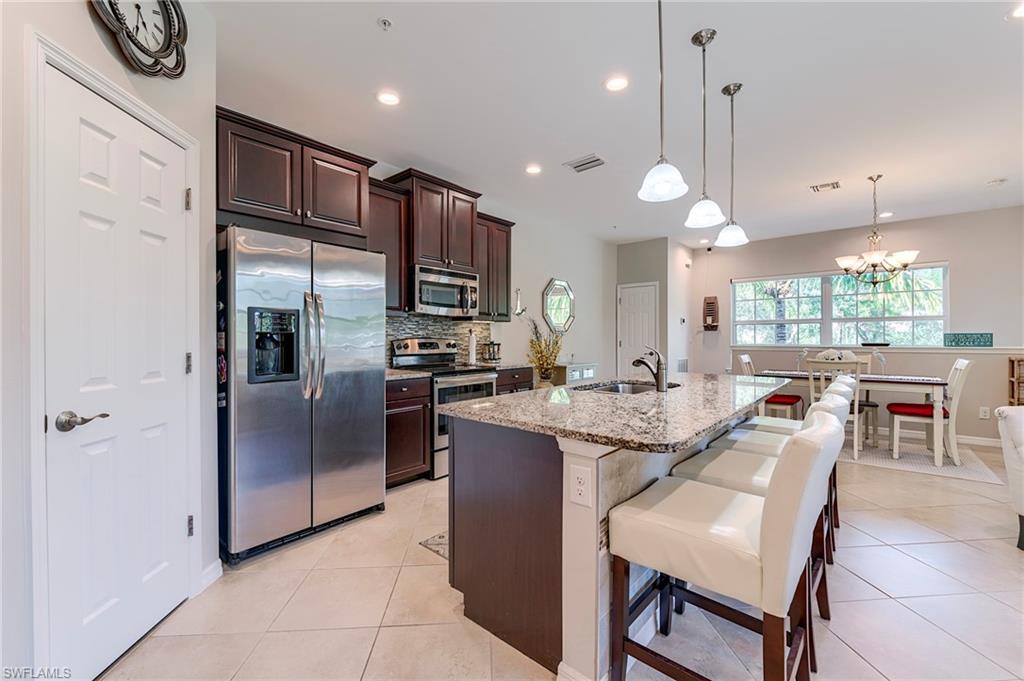 Kitchen with dark brown cabinets, appliances with stainless steel finishes, light stone counters, pendant lighting, and an island with sink