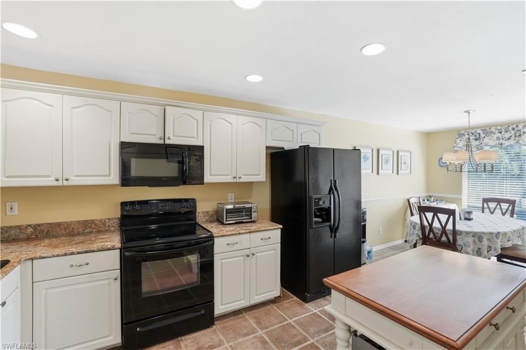 Kitchen with black appliances, white cabinets, decorative light fixtures, a center island, and a chandelier