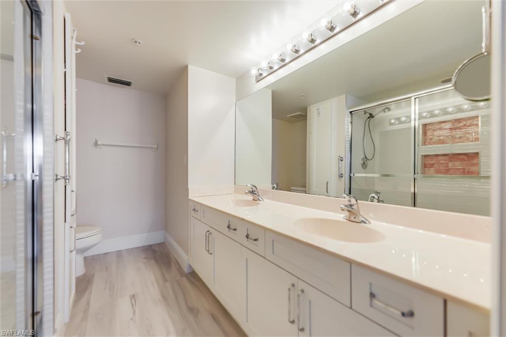 Full bathroom with double vanity, a stall shower, and light wood-style flooring