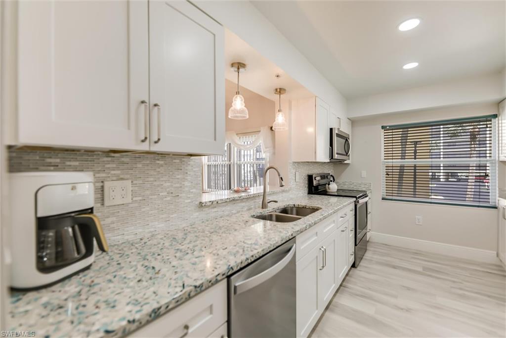 Kitchen featuring appliances with stainless steel finishes, decorative backsplash, white cabinetry, recessed lighting, and light stone counters