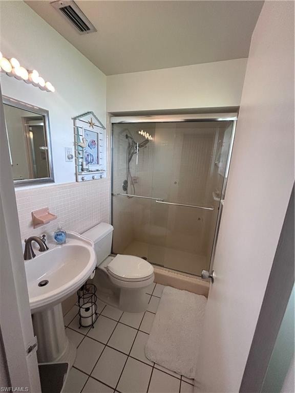 Full bath with light tile patterned flooring, tile walls, a stall shower, and wainscoting
