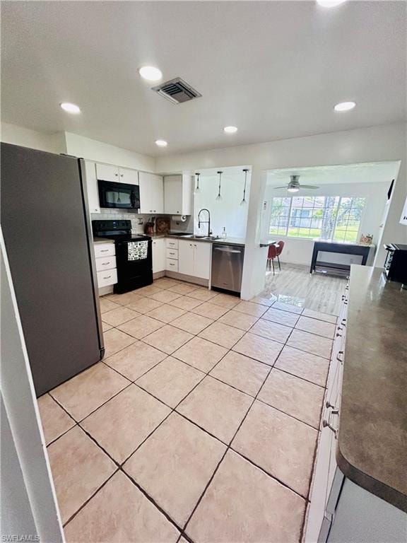 Kitchen with black appliances, white cabinets, dark countertops, light tile patterned floors, and recessed lighting