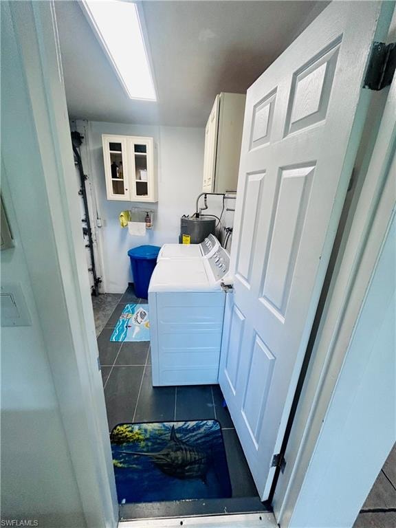 Washroom with dark tile patterned flooring, washer and dryer, and water heater