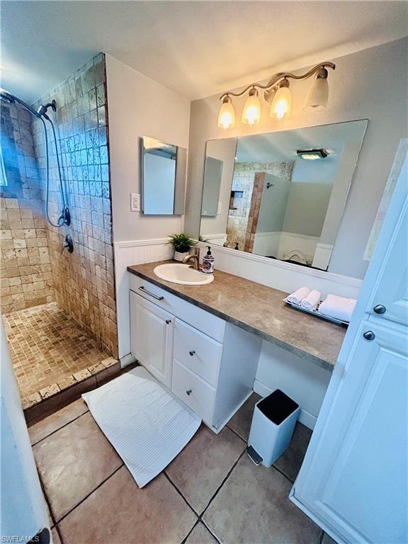 Bathroom featuring light tile patterned floors, vanity, tiled shower, and wainscoting