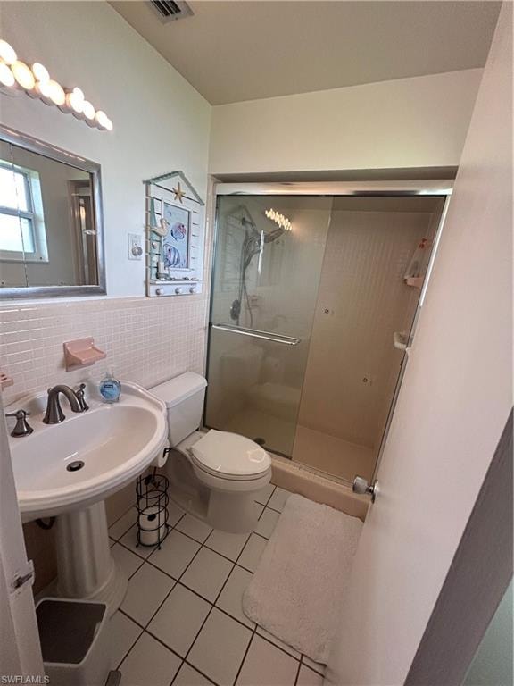 Bathroom featuring light tile patterned floors, tile walls, a stall shower, and a wainscoted wall