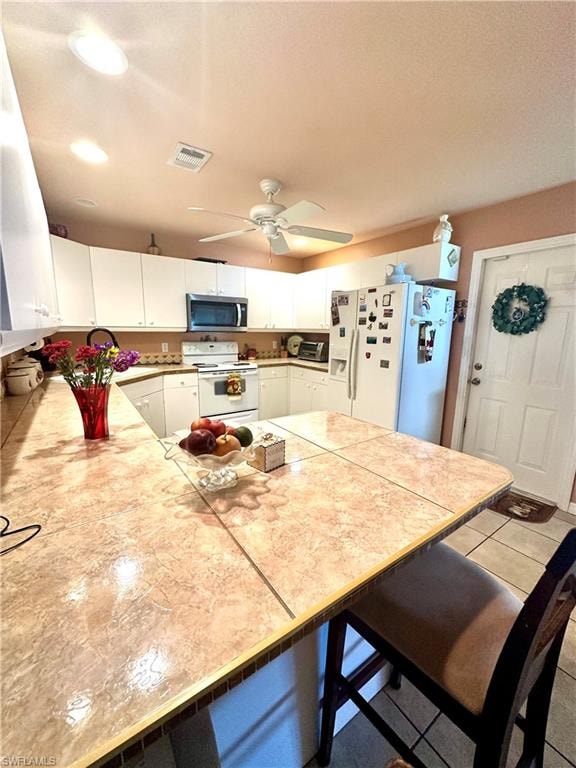Kitchen featuring white cabinetry, a kitchen bar, white appliances, light tile patterned flooring, and a ceiling fan