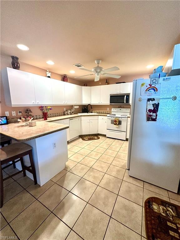 Kitchen featuring white appliances, white cabinetry, light tile patterned floors, a kitchen bar, and recessed lighting