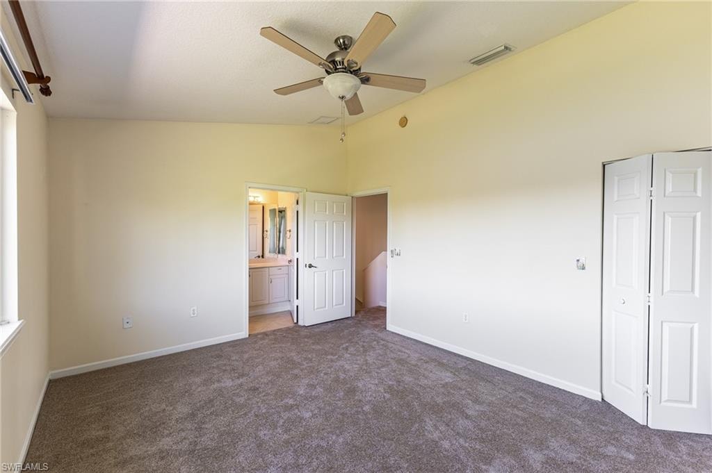 Unfurnished bedroom featuring dark colored carpet, a ceiling fan, ensuite bathroom, and high vaulted ceiling