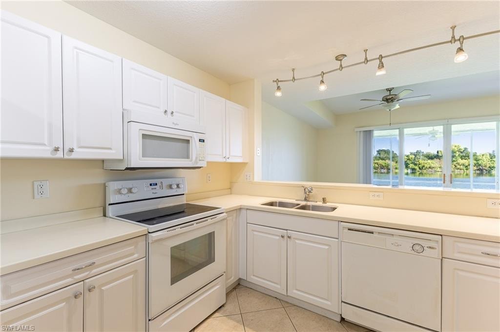 Kitchen with white appliances, white cabinets, light countertops, light tile patterned floors, and a ceiling fan