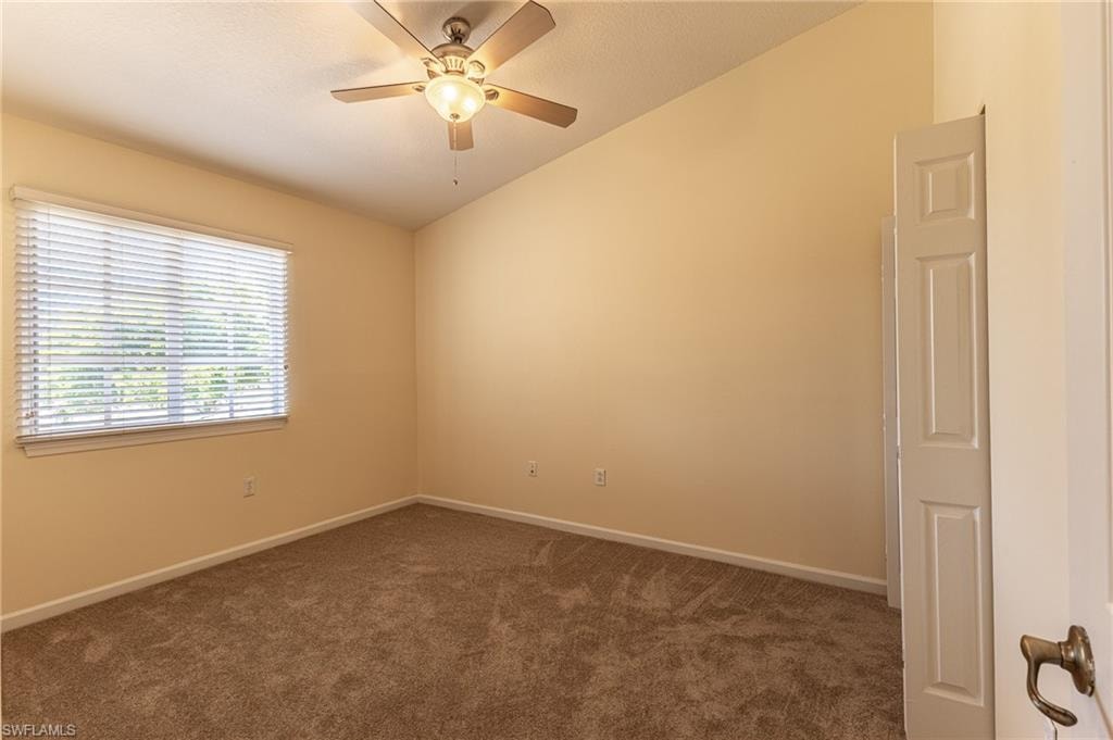 Spare room with vaulted ceiling, dark colored carpet, and ceiling fan