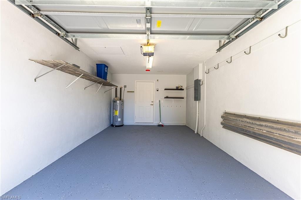 Garage featuring electric water heater, electric panel, and a garage door opener