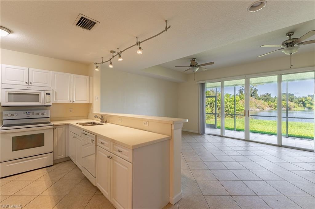 Kitchen with white appliances, light tile patterned floors, a peninsula, a water view, and white cabinetry