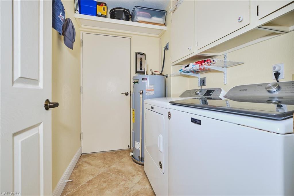 Laundry area with water heater, independent washer and dryer, cabinet space, and light tile patterned floors