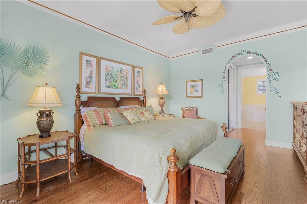 Bedroom featuring light wood finished floors, arched walkways, crown molding, a ceiling fan, and ensuite bathroom