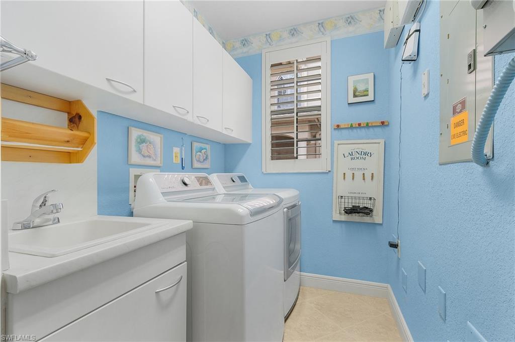 Washroom featuring cabinet space, electric panel, washer and dryer, and light tile patterned floors