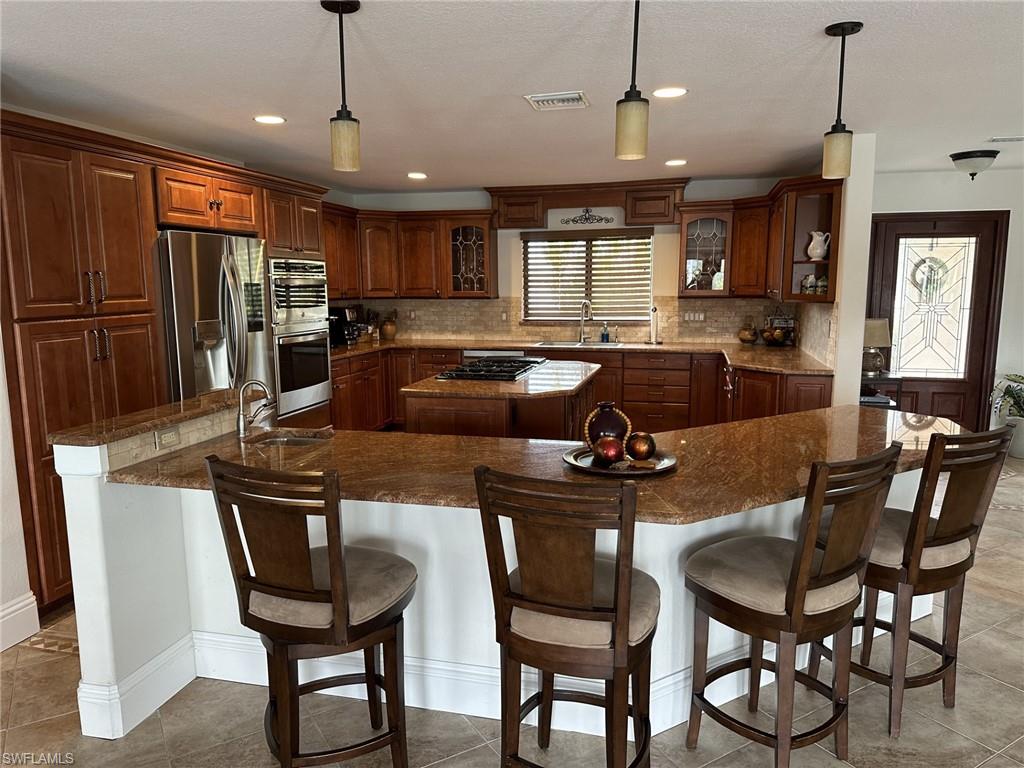 Kitchen featuring a kitchen island, pendant lighting, appliances with stainless steel finishes, glass insert cabinets, and dark stone counters