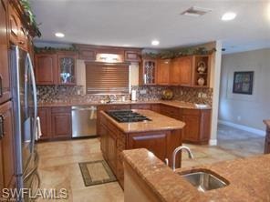 Kitchen with backsplash, glass insert cabinets, brown cabinetry, and recessed lighting