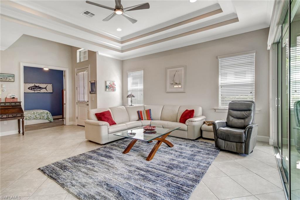 Living room featuring ceiling fan, a raised ceiling, light tile patterned floors, and a healthy amount of sunlight