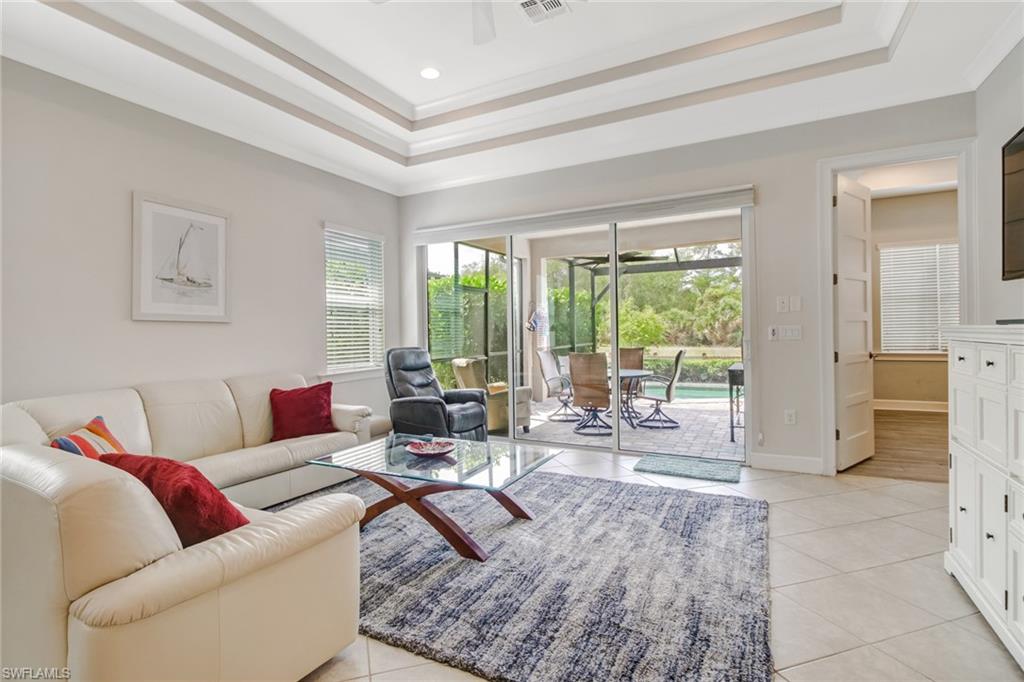 Living room with ornamental molding, a tray ceiling, ceiling fan, and light tile patterned floors