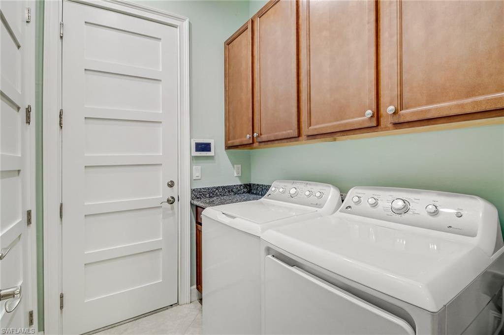 Clothes washing area featuring light tile patterned flooring, washing machine and clothes dryer, and cabinets