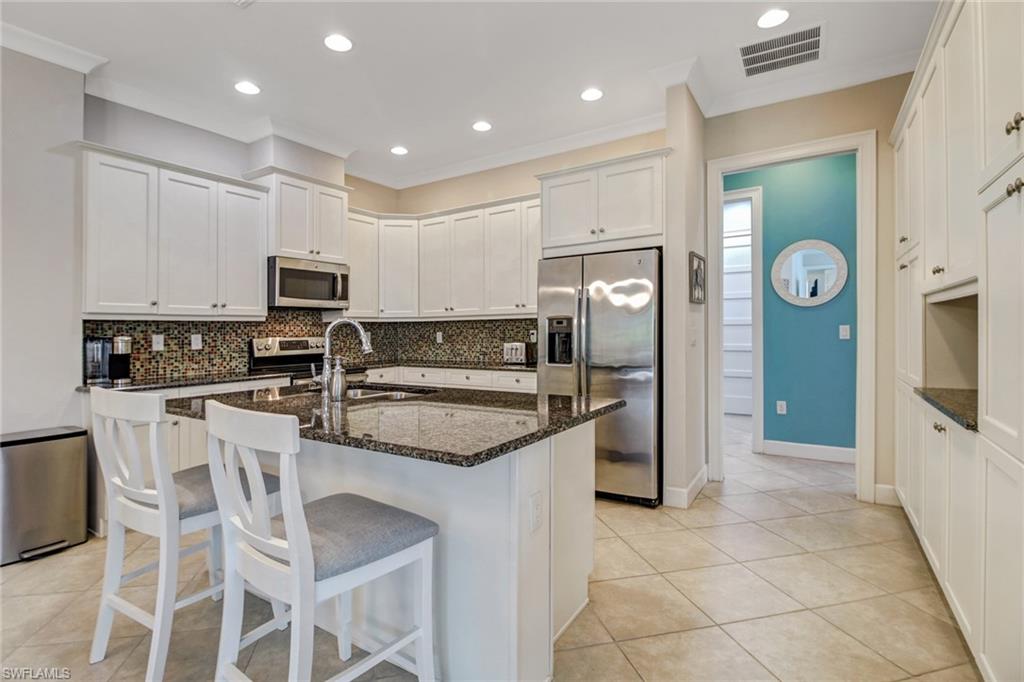 Kitchen with appliances with stainless steel finishes, dark stone countertops, white cabinetry, ornamental molding, and sink