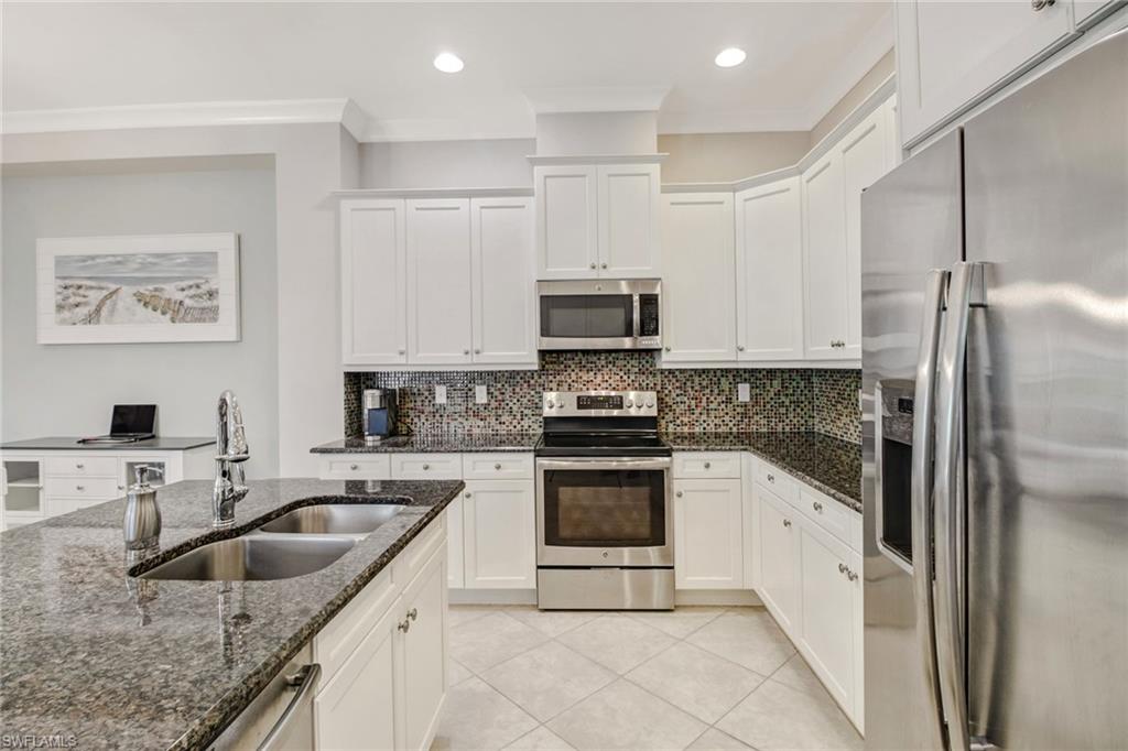 Kitchen with sink, white cabinetry, stainless steel appliances, dark stone counters, and crown molding