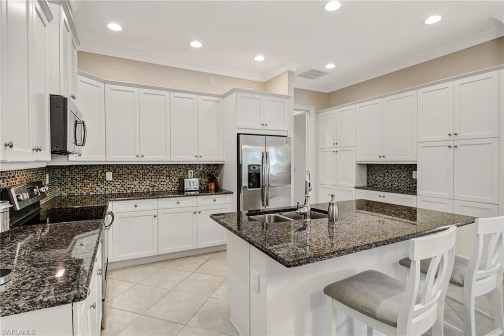 Kitchen featuring dark stone counters, a center island with sink, white cabinetry, and stainless steel appliances