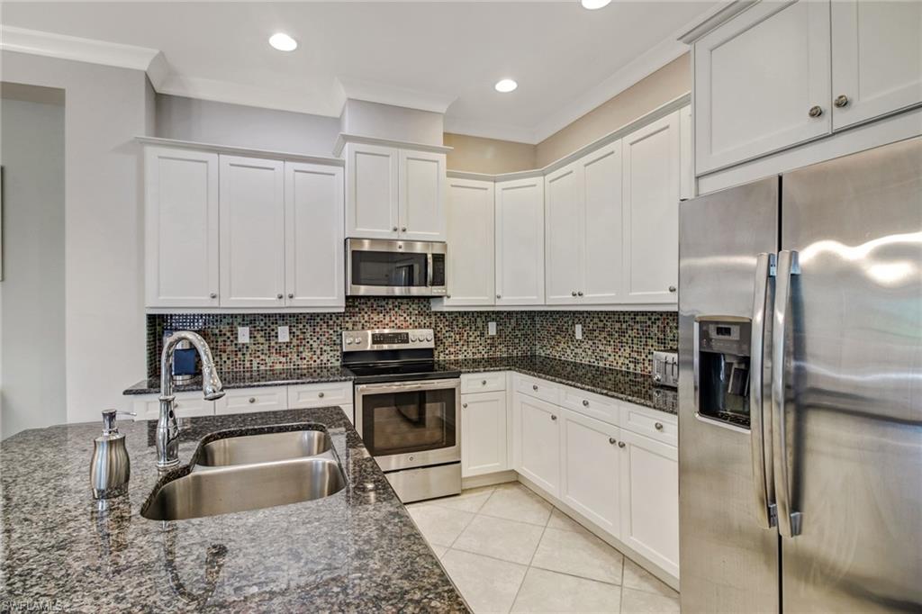 Kitchen with dark stone counters, stainless steel appliances, white cabinets, and sink