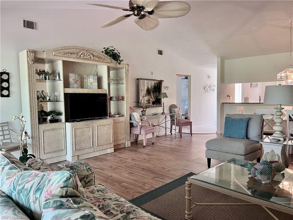 Living room featuring high vaulted ceiling, ceiling fan, and wood-style laminate flooring