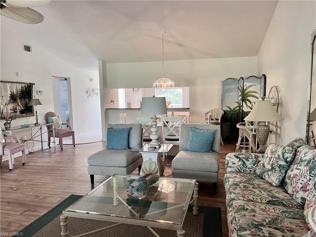 Living room with ceiling fan with notable chandelier, high vaulted ceiling, and wood-style laminate flooring