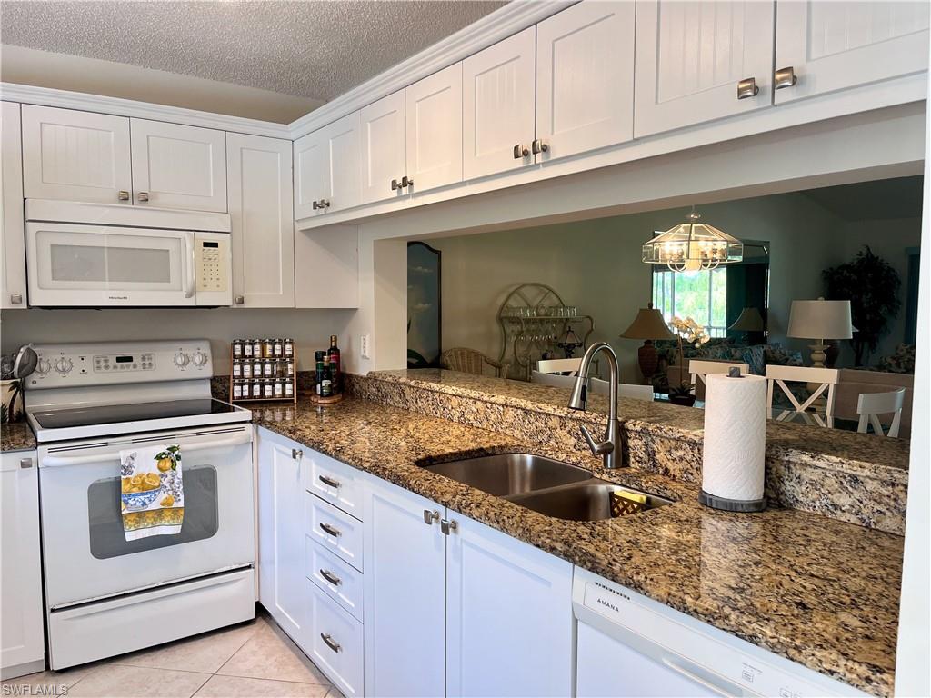 Kitchen featuring a textured ceiling, white appliances, sink, and white cabinets