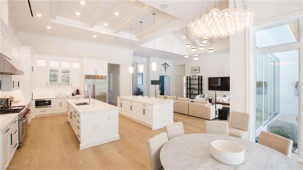 Kitchen featuring built in appliances, tasteful backsplash, an island with sink, white cabinetry, and a notable chandelier