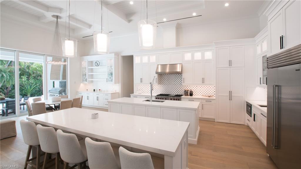 Kitchen featuring stainless steel appliances, wall chimney exhaust hood, beamed ceiling, backsplash, and a kitchen island with sink