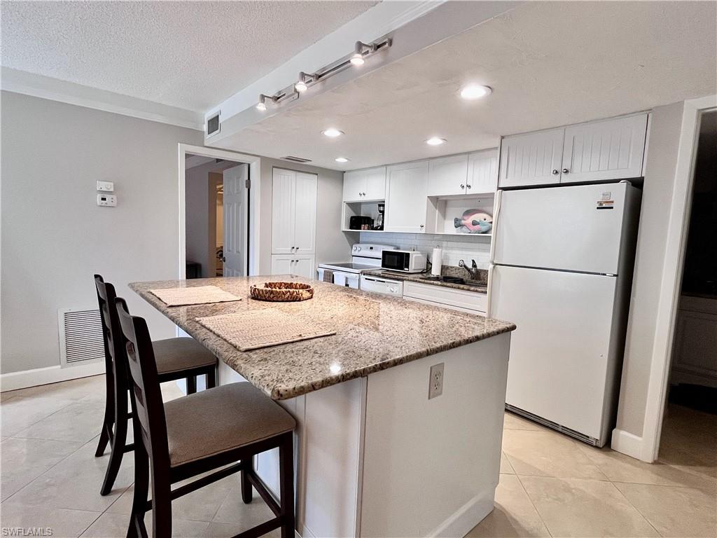 Kitchen with light stone counters, white appliances, a breakfast bar, white cabinets, and light tile floors
