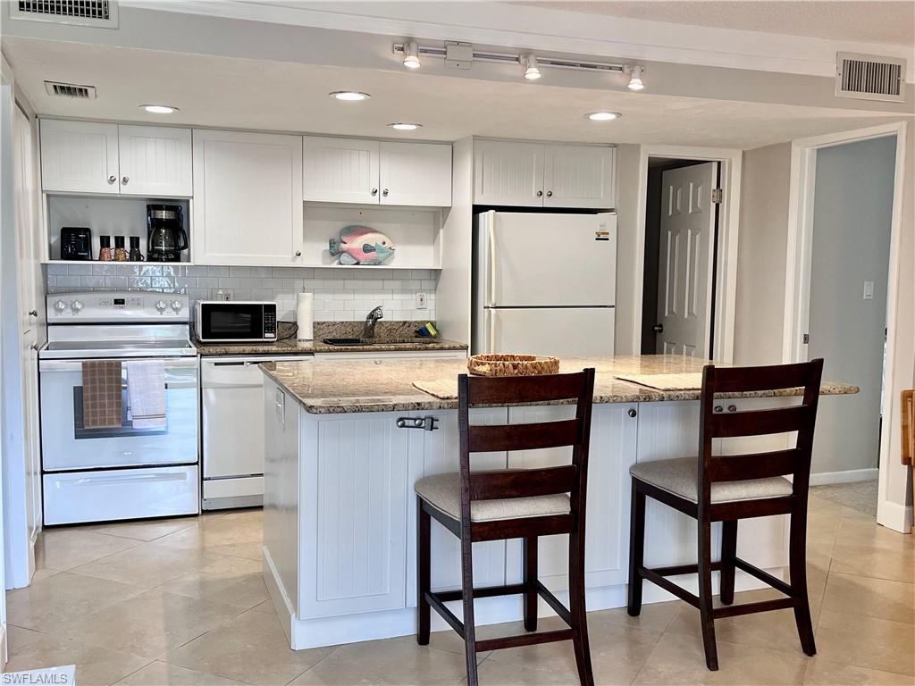 Kitchen with white appliances, white cabinetry, light stone counters, open shelves, and recessed lighting