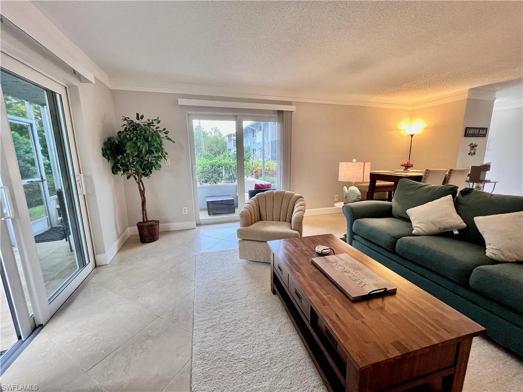 Living area featuring healthy amount of natural light, a textured ceiling, crown molding, and light tile flooring