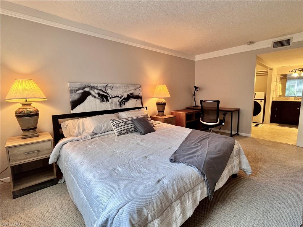 Primary Bedroom with light colored berber carpet, crown ornamental molding, office desk and large walk in closet including washer/dryer combination unit, and ensuite bath with shower.