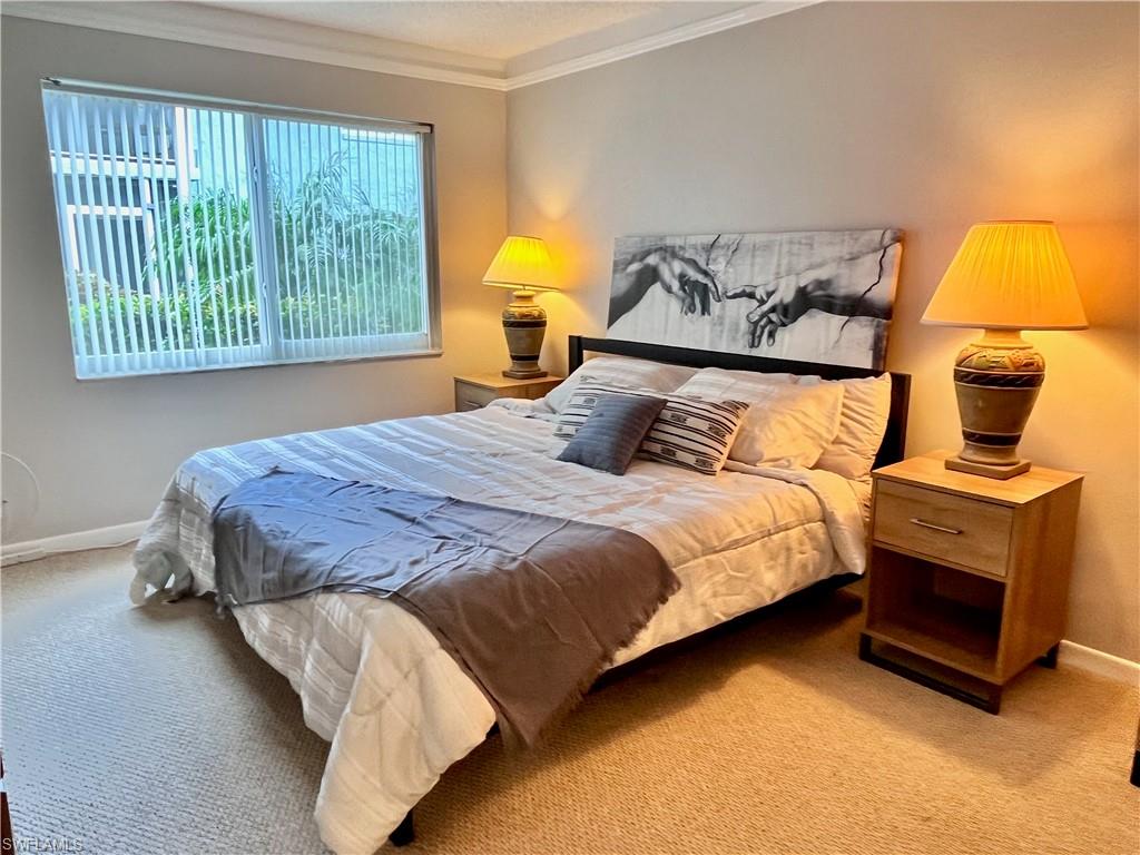 Primary bedroom with berber carpet, crown ornamental molding, and a King bed with an office desk for working.