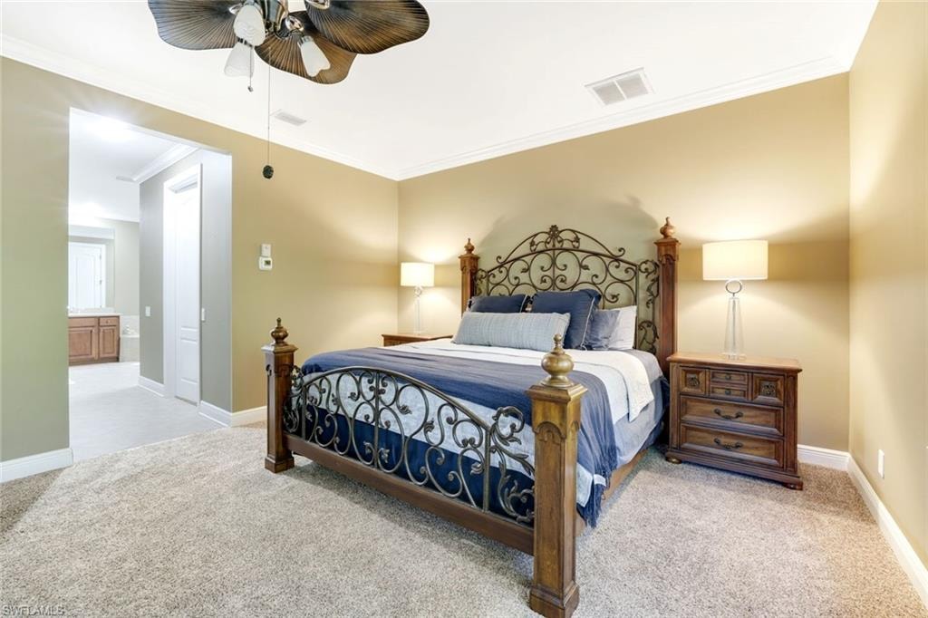 Bedroom with light colored carpet, ornamental molding, a ceiling fan, and ensuite bath
